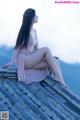 A woman in a pink dress sitting on a roof.