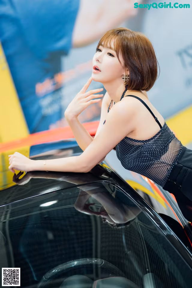 A woman leaning on the hood of a black car.