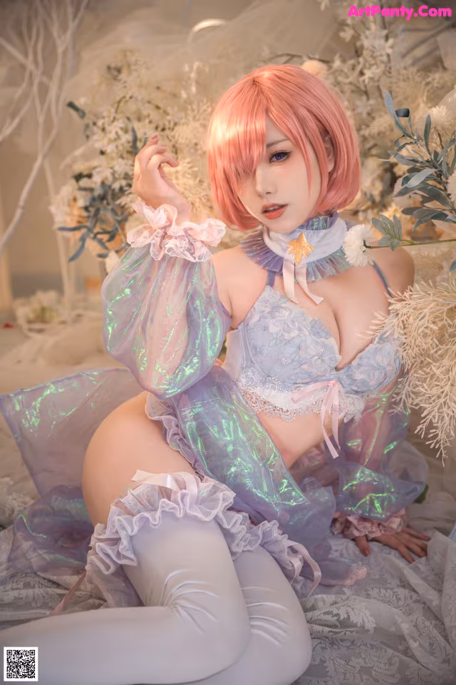 A woman with pink hair sitting on a bed.