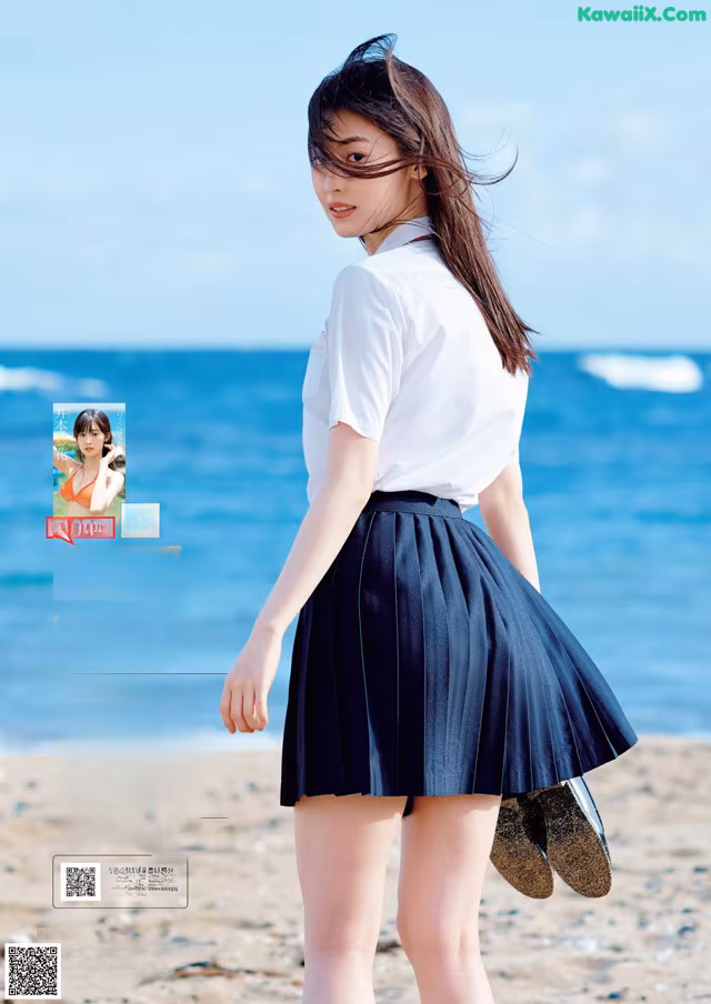 A woman in a white shirt and black skirt standing on a beach.