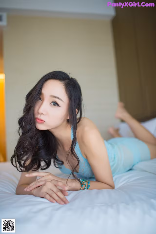 A woman laying on a bed in a blue dress.
