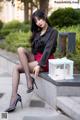 A woman in a black shirt and red skirt sitting on a ledge.