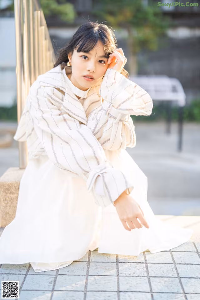 A woman in a white dress sitting on a bench.