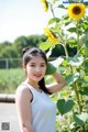 A woman standing next to a tall sunflower in a field.