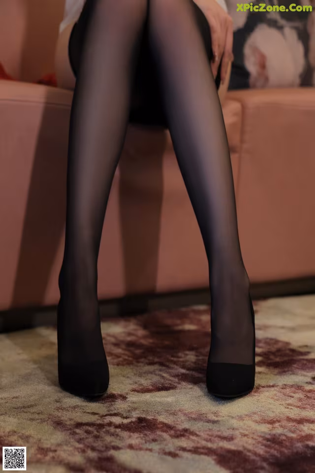 A woman sitting on a couch wearing black stockings and high heels.