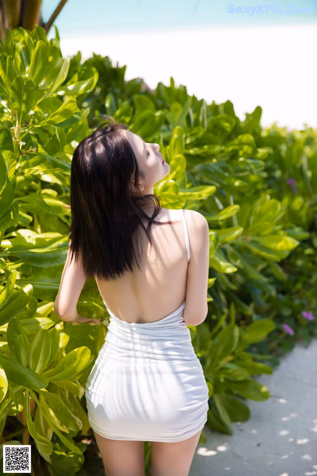 A woman in a white dress standing on a sidewalk.