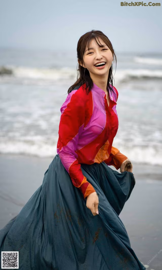 A woman in a colorful shirt and skirt on the beach.