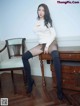 A woman sitting on top of a wooden desk next to a chair.