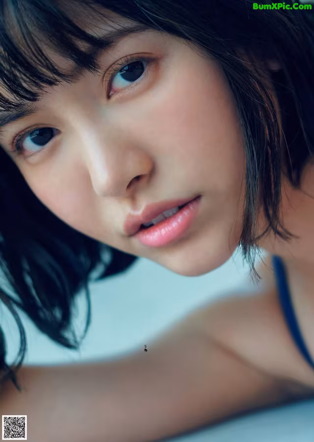 A woman with long black hair and blue eyes laying on a bed.