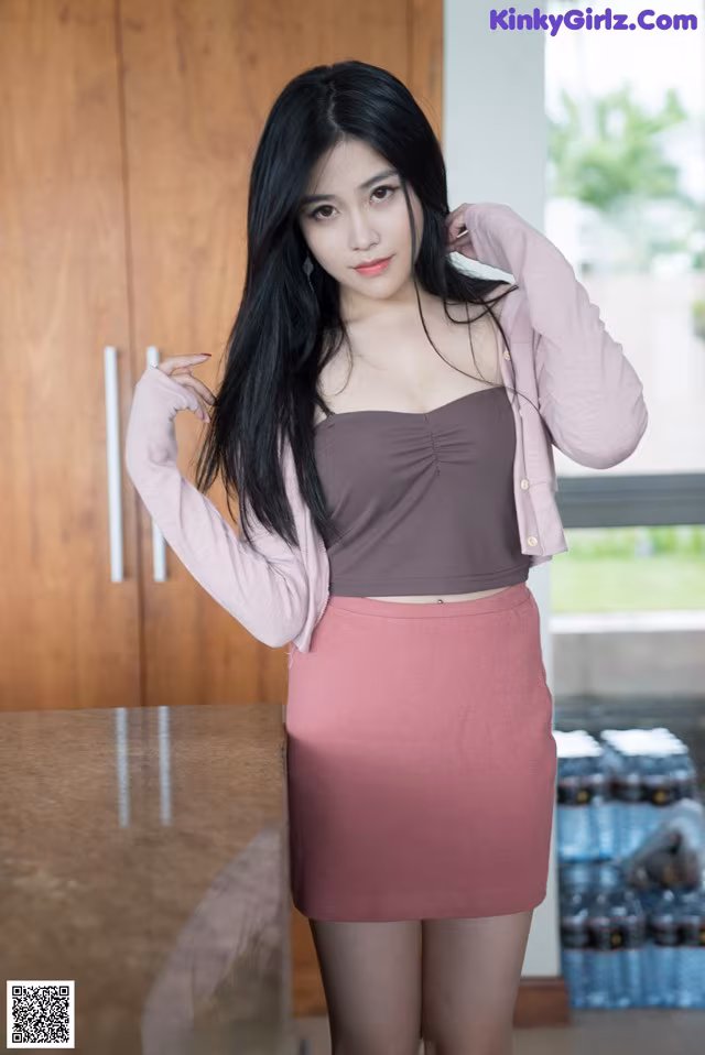 A woman in a pink skirt and a brown top posing for a picture.