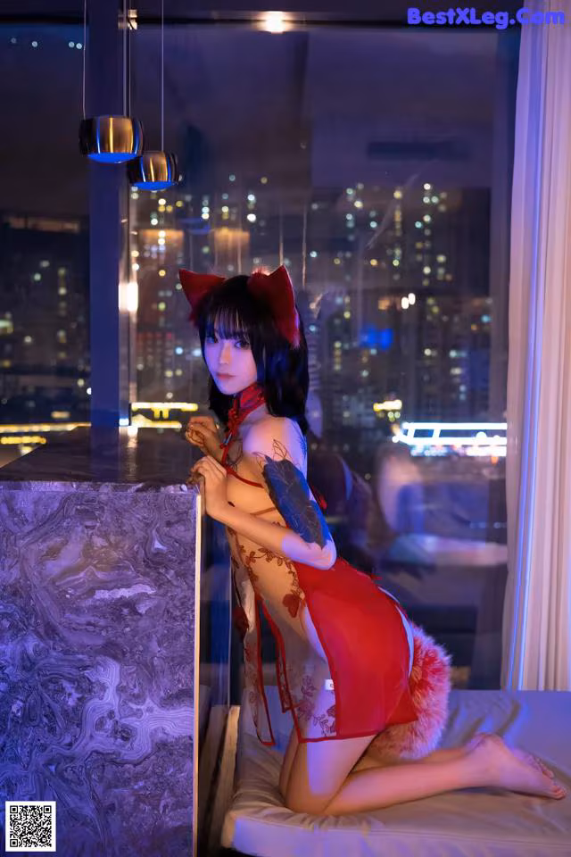 A woman in a red dress sitting on a bed.