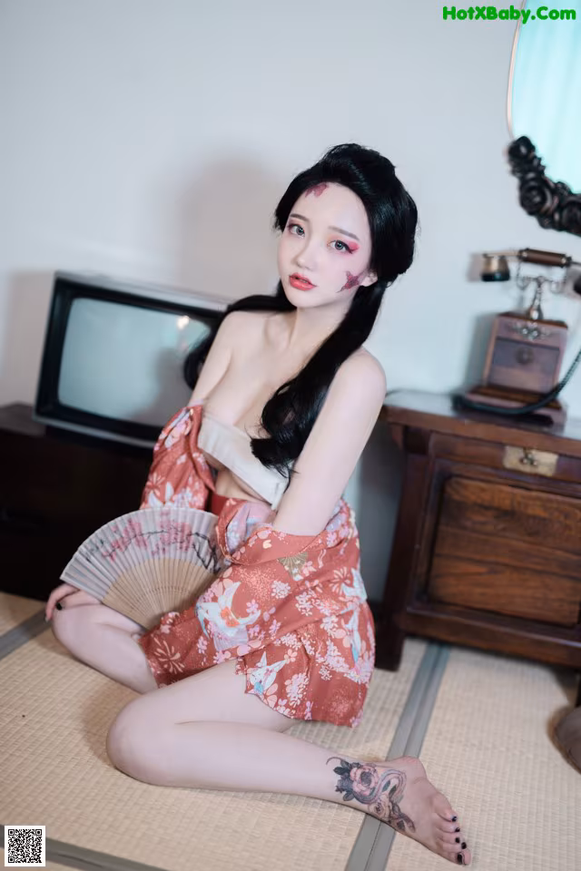 A woman in a kimono sitting on the floor with a fan.