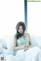 A woman sitting on a bed in front of a window.