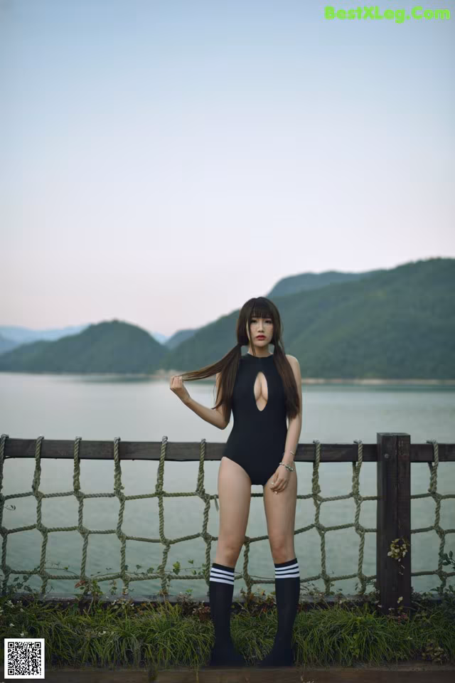 A woman in a black bathing suit standing by a fence.