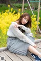 A woman sitting on a wooden bench in front of yellow flowers.