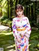 A woman in a white kimono standing in a garden.